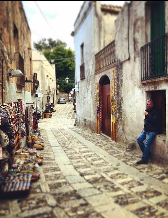 A cobblestoned narrow street with small craft shops displaying goods outside in Sicily