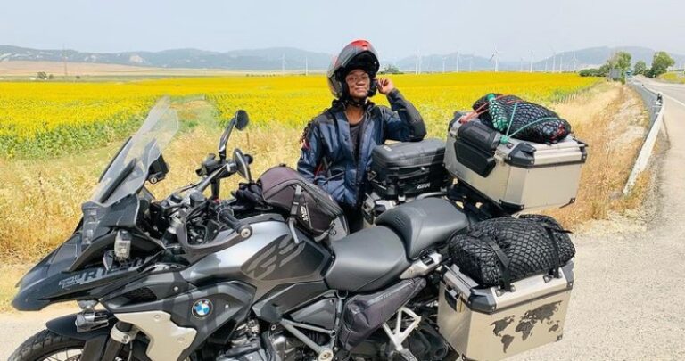 A female motorcyclist standing behind a fully packed motorcycle in a sunflower field- Gift ideas