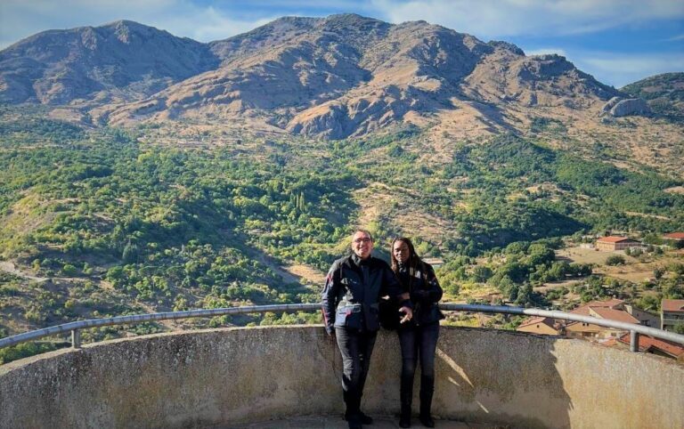 A couple in motorcycle gear with the view of a mountain range behind them
