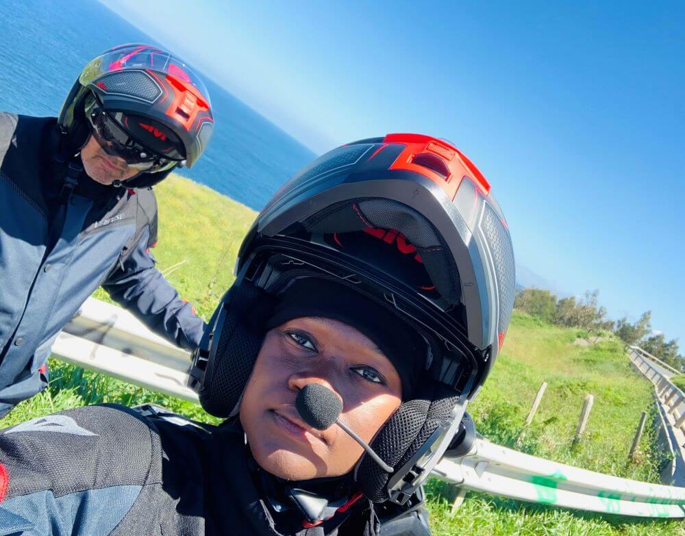 A motorcycle couple in full gear. The female is in front of the bike and the male is behind