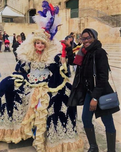 The diversity of Malta. A Maltese woman dressed in elaborate medieval costume on the left and a black tourist on the right