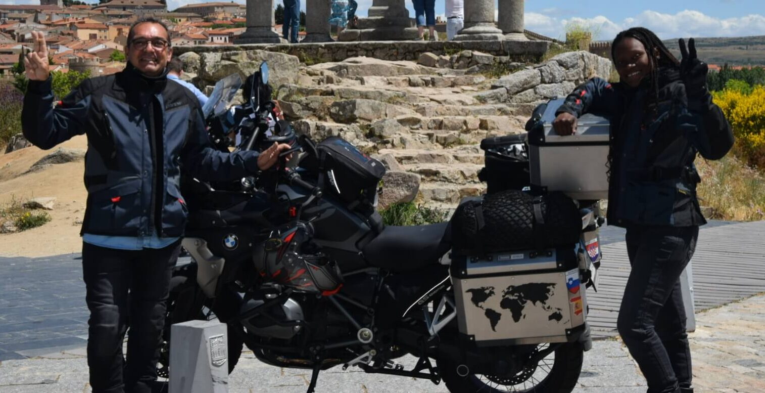 Couple in full motorcycle gear standing next a motorcycle outside