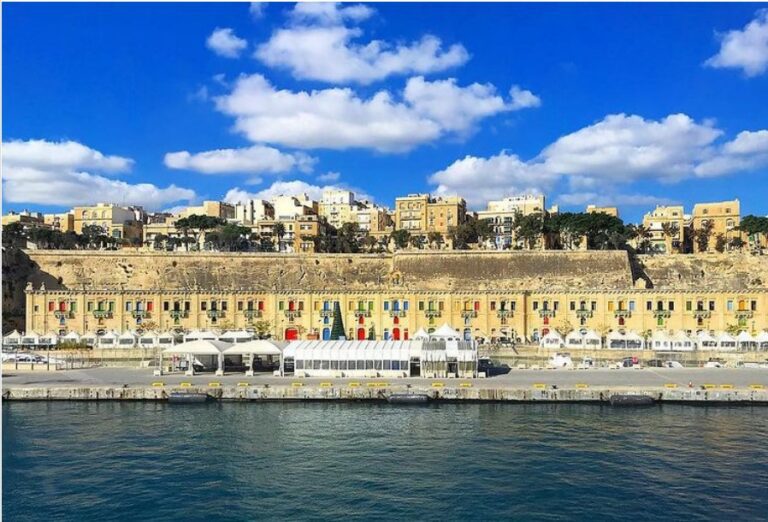 A harbour in the Mediterranean Island of Malta with an imposing building with colourful balconies and the urban landscape behind