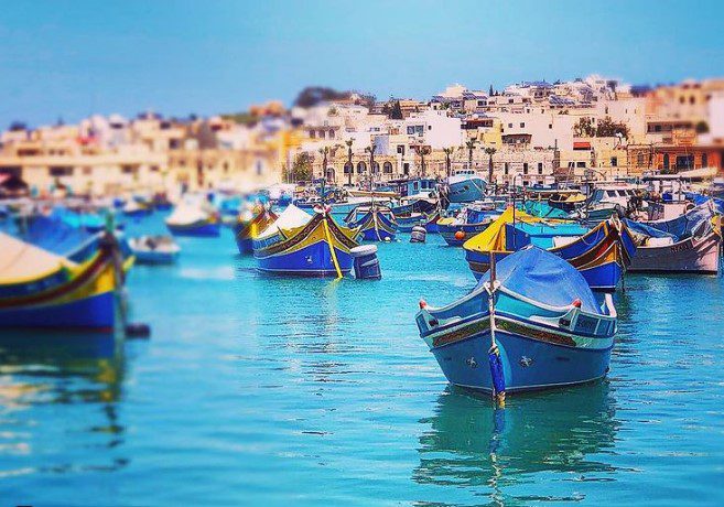 Local boats on the sea with The Fishing Village of Marsaxlokk in the South of Malta