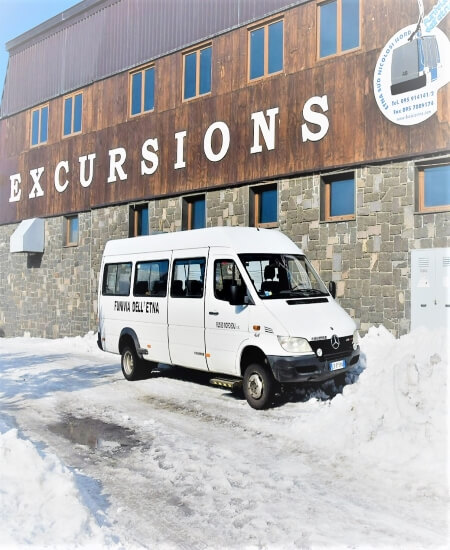 A van next to a building with the word "excursions" at the base of the volcanic mount Etna, a low-budget winter destination