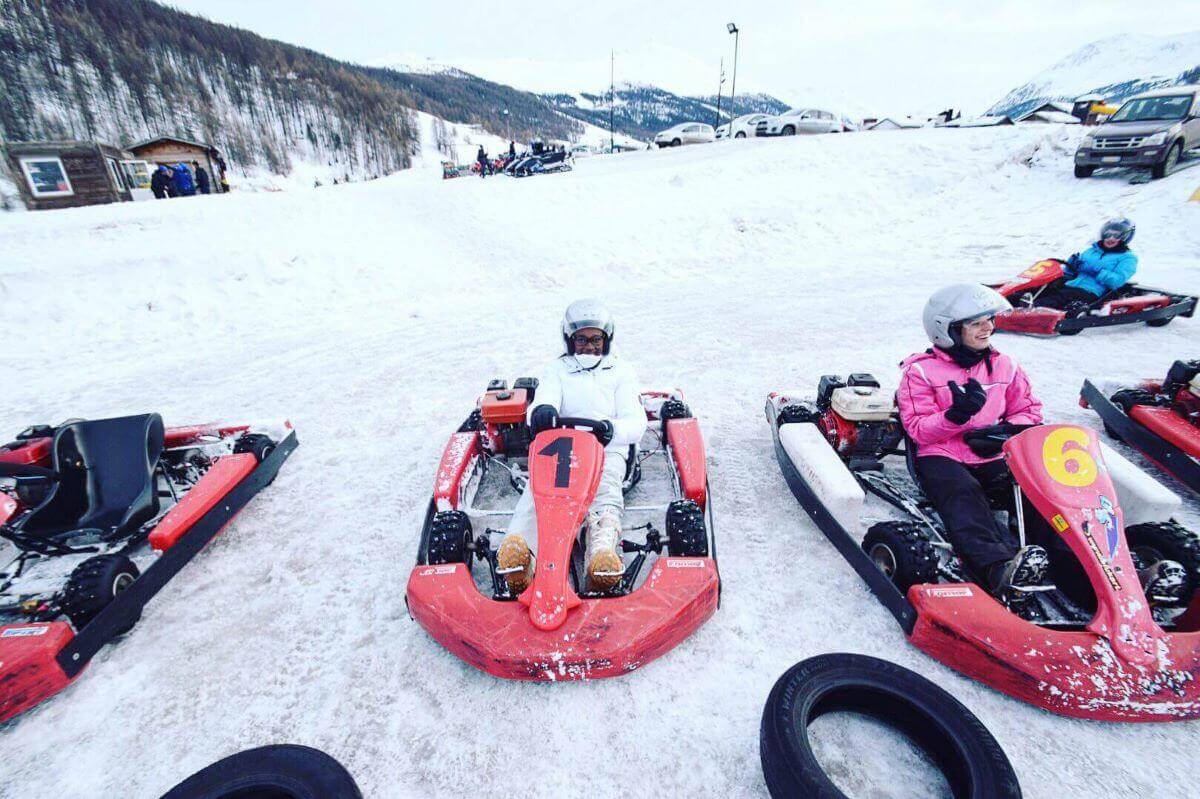 Go-karts with drivers in them on a snowy track with a view of the snow-capped mountain behind- Low-budget winter destinations in Italy