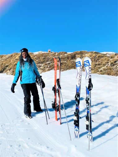 A female skier with 2 pairs of skis vertically stuck in the snow and the mountain behind her in Roccaraso, a low-budget winter destination in Italy