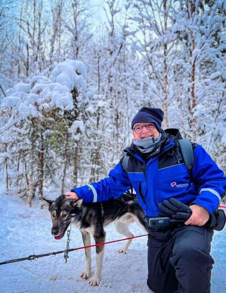 A man in winter gear, kneeling outdoors and petting a black husky in Rovaniemi Lapland