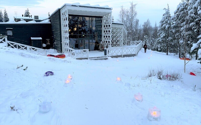 A hotel reception built of wood and glass, in the arctic with lights lining the snow-covered path