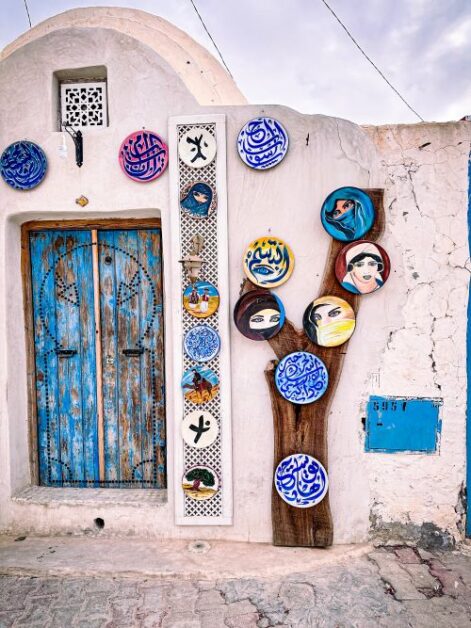 A what wall decorated with a mural of several, colourful female faces. On the left, there is a blue door