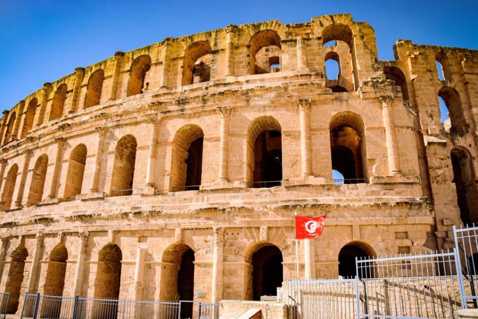 A roman amphitheater with the flag of Tunisia in front of it.