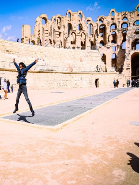 A woman in a jumping pose inside the arena of an amphitheatre in Tunisia
