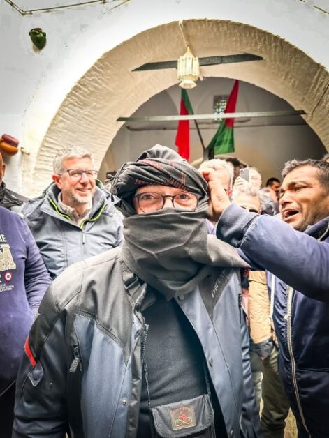A man getting turbaned by another man with onlookers observing