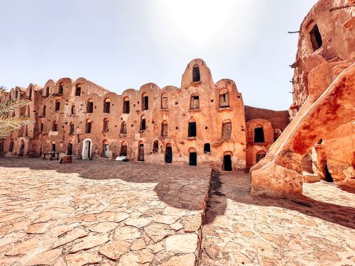 A courtyard of a structure made of mud, three storeys high, with stairs in front of them.
