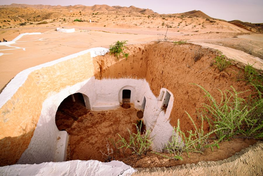 The courtyard of an underground cave dwelling in the Sahara. There are several oval doorways and it is painted white