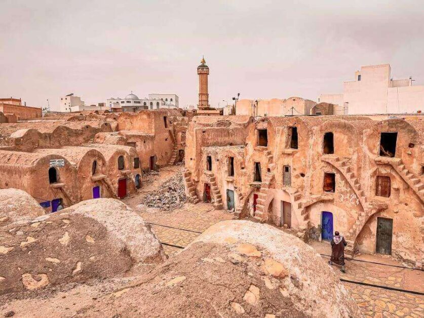 A courtyard of a structure made of mud, three storeys high, with stairs in front of them.