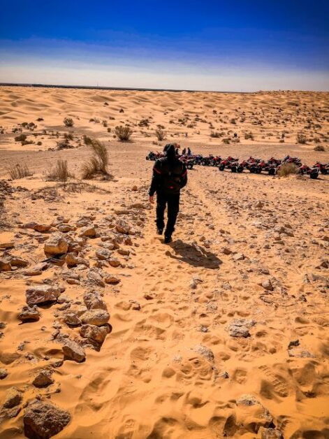 The back view of a man in the desert, walking towards a group of parked quad bikes