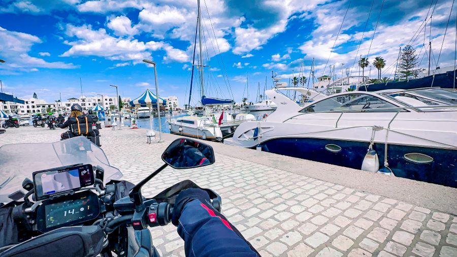 The point ov view of a motorcyclist riding in a marina with yachts berthed in the bay