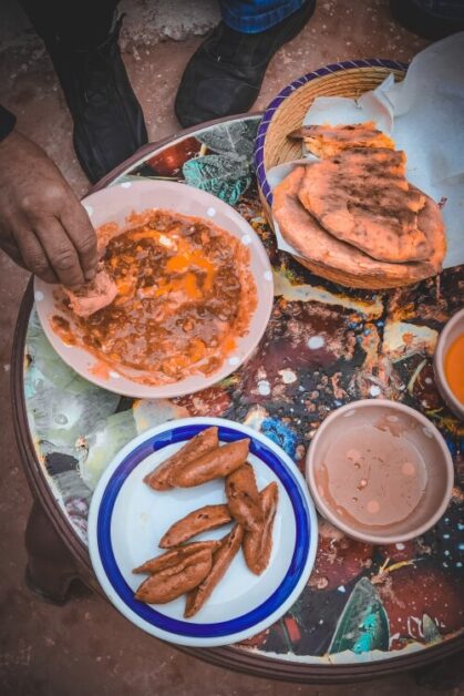A large round tray with 5 bowls of food. You can see a hand dipping bread in a sauce