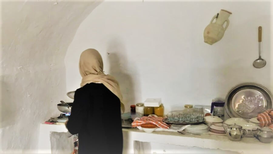 The back view of a woman in a kitchen with utensils on a tabletop
