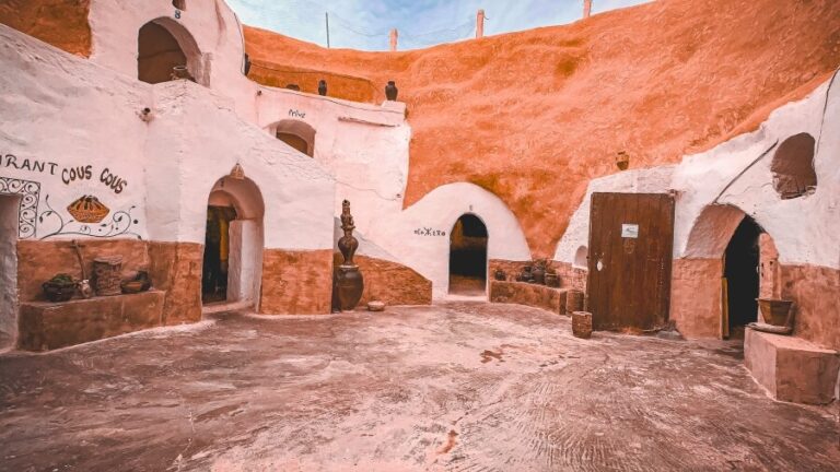 A circular courtyard of an underground cave hotel with arched doorways, wooden doors and clay pots