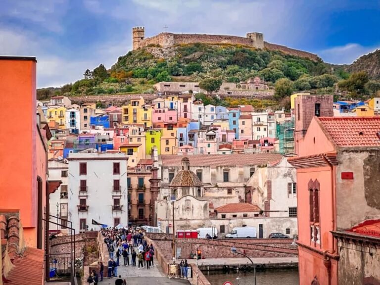 A colourful hillside town with the backdrop of a large walled castle atop a hill
