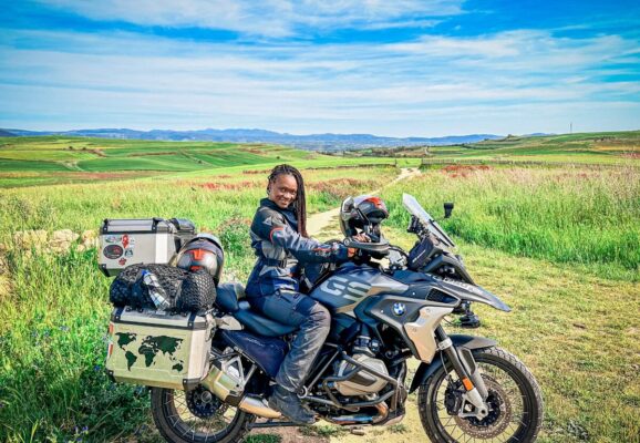 A black female motorcyclist on a big motorcycle parked in a large field