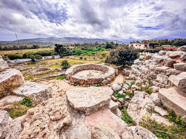 An archeological site with circular rock structures, half if the ruins in an open landscape with hills in the background