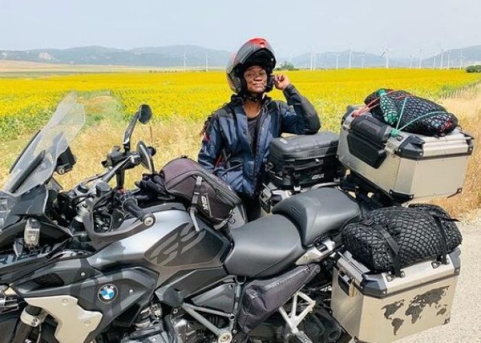 A female motorcyclist standing behind a fully packed motorcycle in a sunflower field- Gift ideas