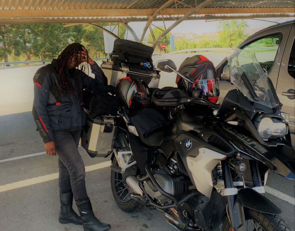 A female motorcyclist standing next to a motorcycle with her hand on her head as if in distress